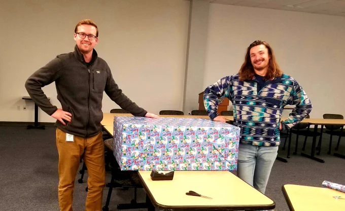 Two people standing next to a large wrapped present.