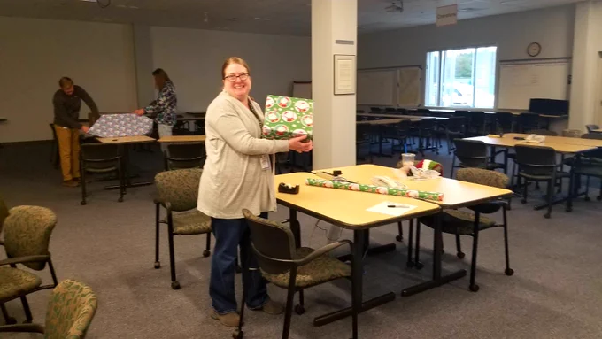 One person holding a wrapped present with people wrapping presents in the background.
