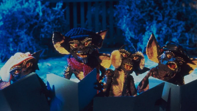 A group of Gremlins holding books, standing in a snowy garden.