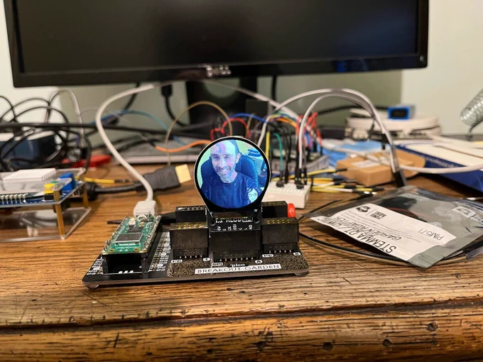 Pico W in a Pimoroni breakout garden with a round LCD display in it. The display shows a Mastodon user’s avatar with another avatar inlaid at the bottom right.