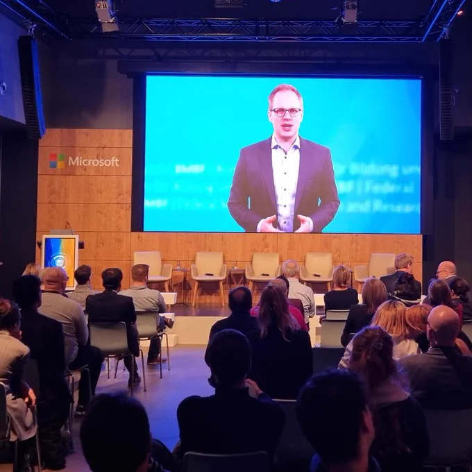 Das Foto zeigt eine Videobotschaft von Dr. Jens Brandenburg, Parlamentarischer Staatssekretär im Bundesministerium für Bildung und Forschung, auf einem Videoscreen auf der Bühne von Microsoft Berlin.
