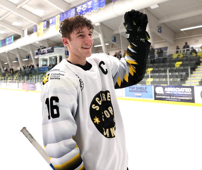 Ryan Tattle on an ice rink, smiling and holding up a hockey gloved-fist.
