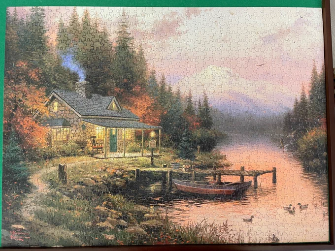 Puzzle with an image of a cabin on a lake with mountains and trees.