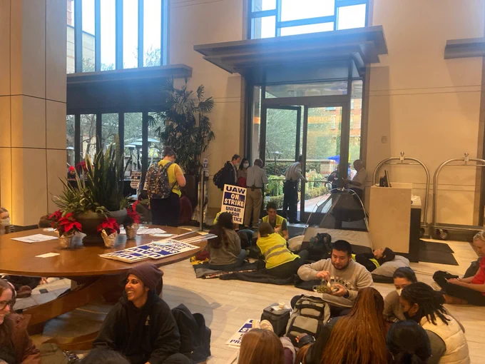 A group of striking Academic Workers occupies the lobby of the UCLA Luskin Conference Center.