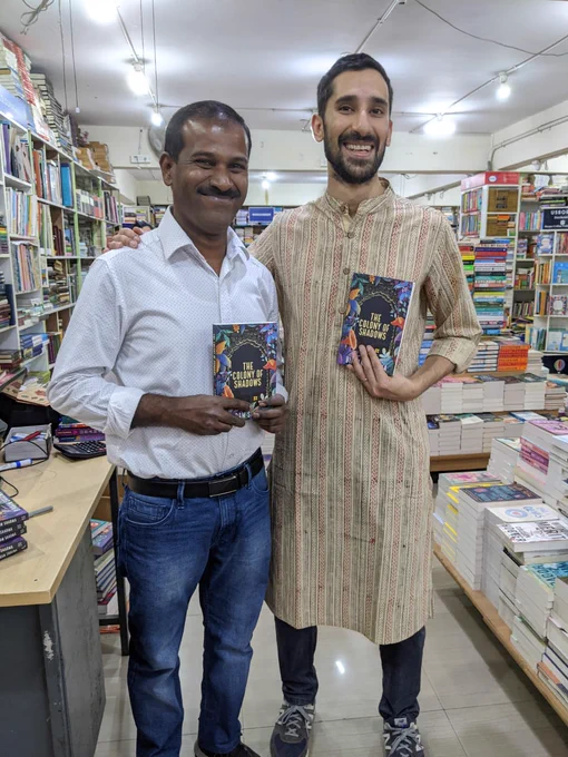 A photo of me and Mayi Gowda posing with my book in Blossoms. Behind us, marvellous piles of books all over the place.