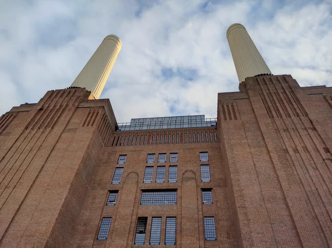 A tall red brick building with two tall round chimneys. View from ground level looking up. 