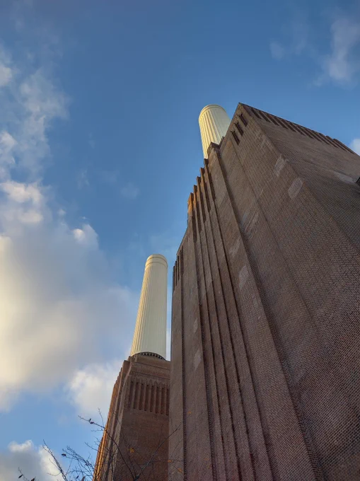 A tall red brick building with two tall round chimneys. View from ground level looking up.