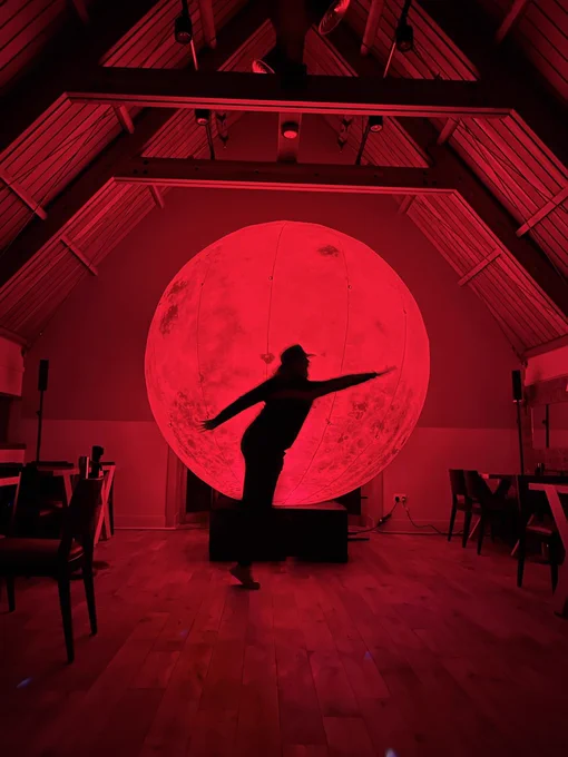 Elspeth Murray in silhouette by a huge red moon at Redcoats Cafe