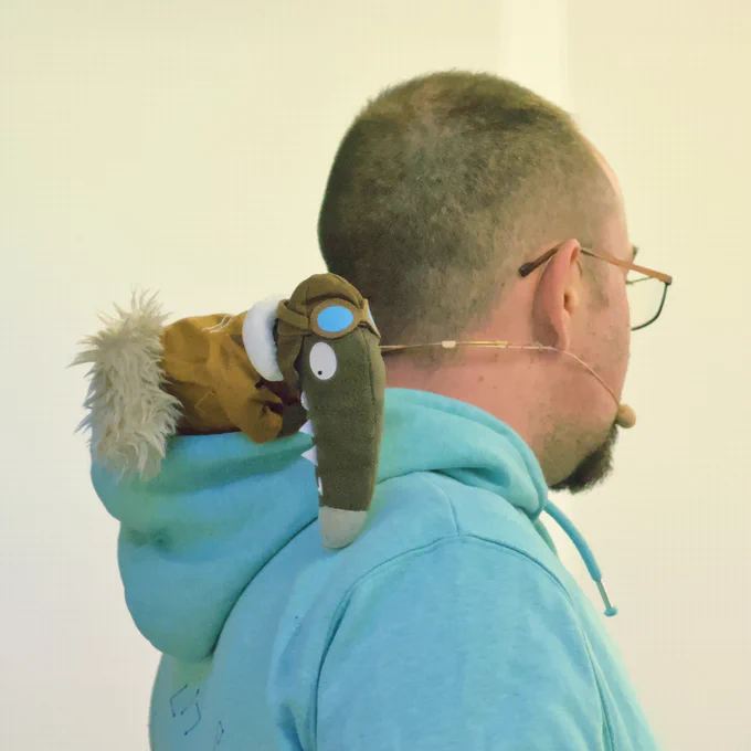 Jérôme Masson vu de dos avec un sweat à capuche dans laquelle se trouve une peluche.