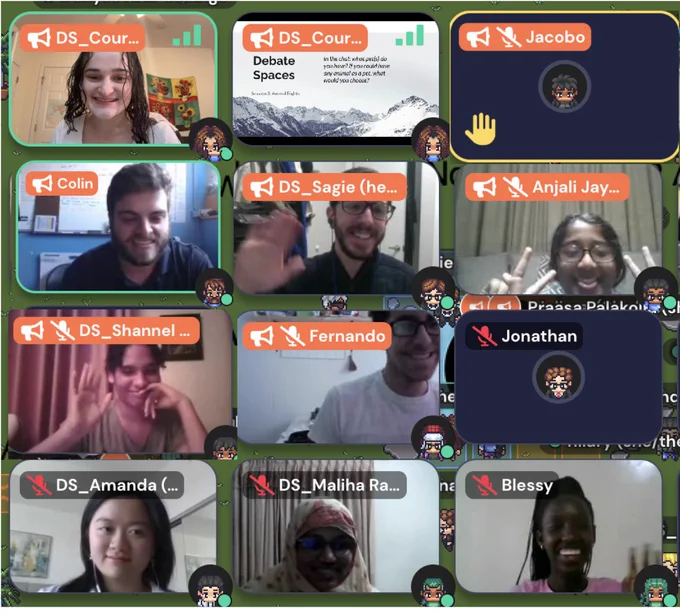 A screenshot of the gather.town space with twelve squares showing students and staff waving, holding up peace signs, raising their virtual hands, and showing the Debate Spaces slide deck. Guest speaker Colin is in the second row on the left side against a blue background with a whiteboard.