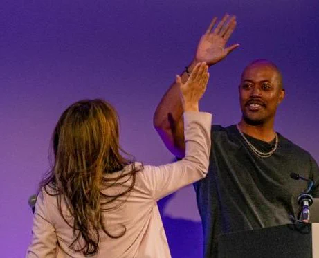 A man and woman high five enthusiastically on stage