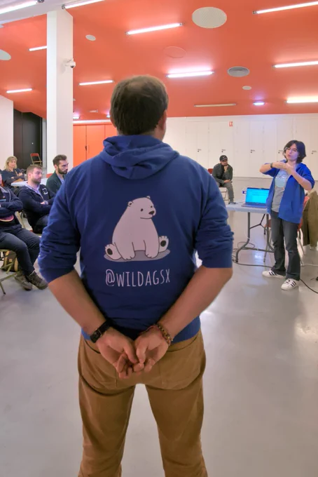 Stéphane Philippart de dos avec un sweat à capuche sur lequel est dessiné un ours assis sous-titré de son compte Twitter