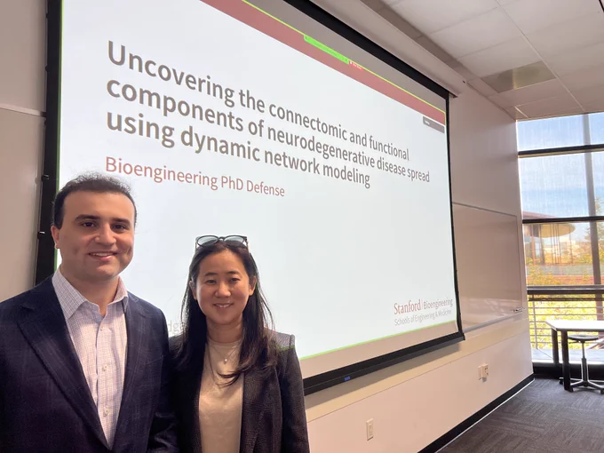 Dr. Dadgar-Kiani and Dr. Lee in front of the title slide of the PhD defense, "Uncovering the connectomic and functional components of neurodegenerative disease spread using dynamic network modeling."
