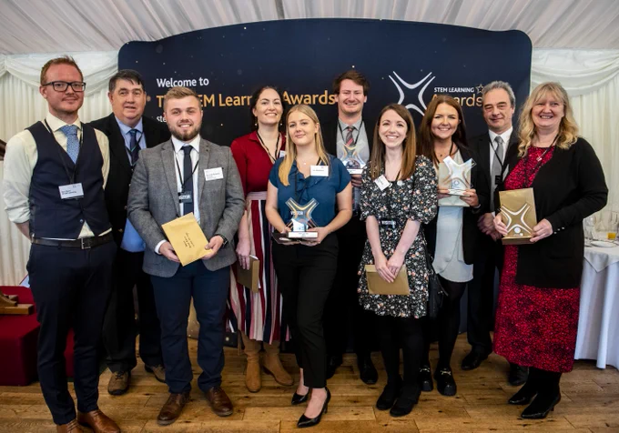 A group of people stand in front of a sign, holding an award.