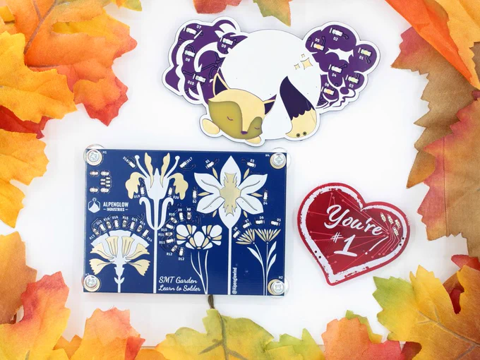 SMT circuit board kits surrounded by autum leaves - a blue SMT Garden with flowers, a purple Foxy Pride, and a red heart "You're #1" PS I Hate You.