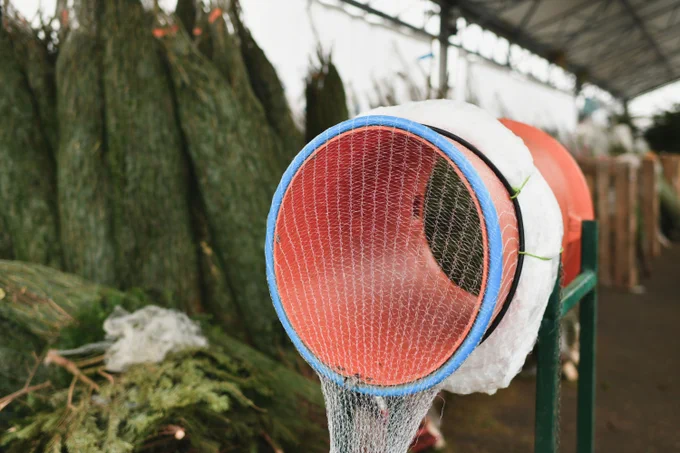 Red christmas tree wrapping device Packed in a plastic net

Christmas tree at a market and wrapping device