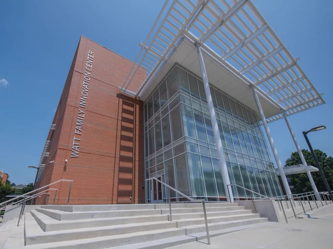 The exterior of a building with many glass windows and a grass field in front of it.