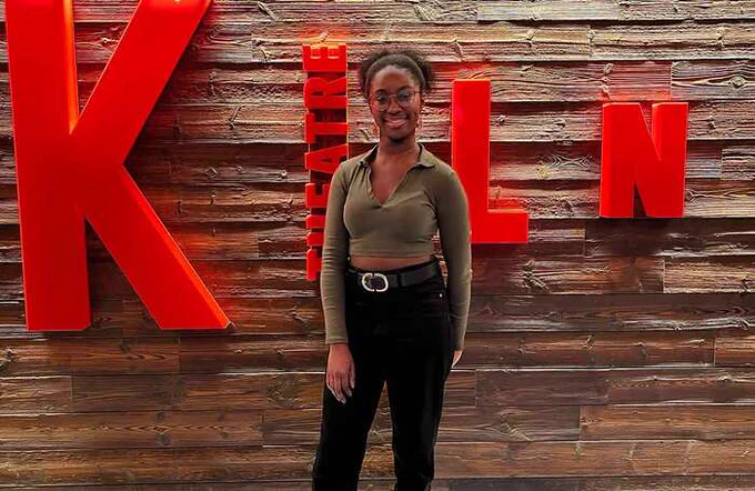 Jessica Mensah in front of the red KILN theatre sign, smiling at the camera