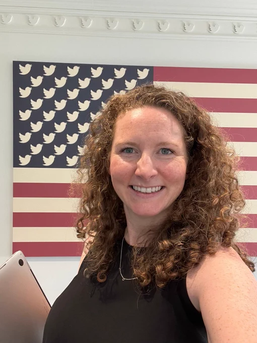 Bridget photographed in front of American flag with Twitter birds at the Washington, DC Twitter office (circa 2022).