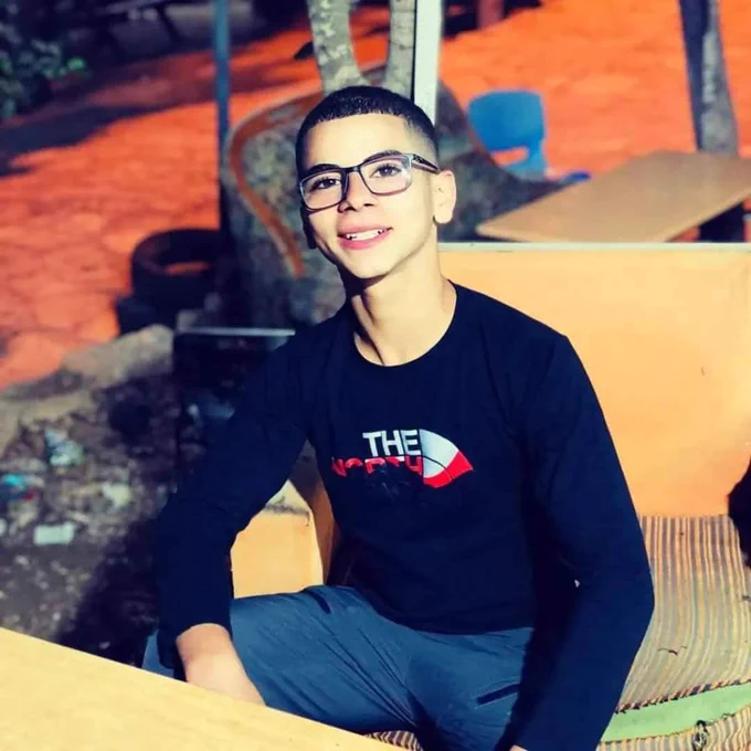 Boy wearing glasses and a long-sleeved shirt smiles while sitting at table