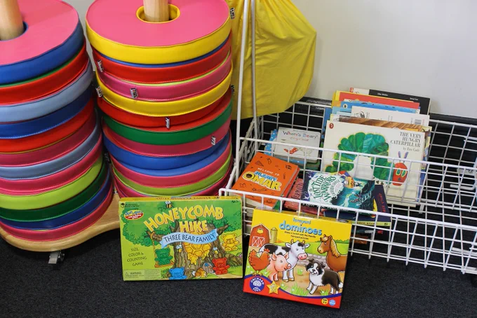 A colourful image of cushions for children to sit on and a variety of children's books and games.