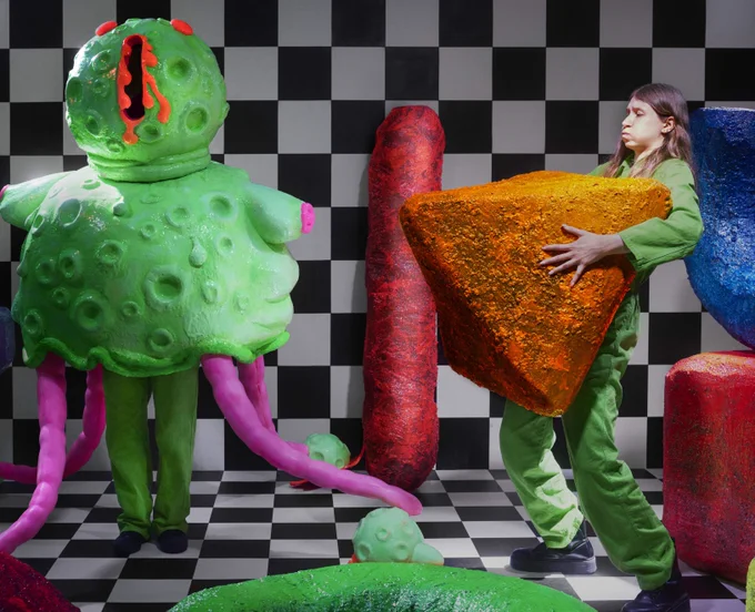 A checkerboard background with inflatable toys and a girl holding a orange triangle 