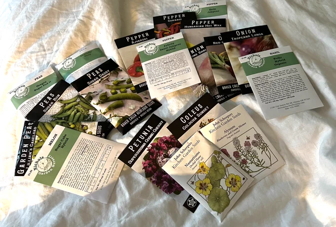 About 20 very well curated seed packets laid out on the bed. Mostly peas, peppers, and onions.