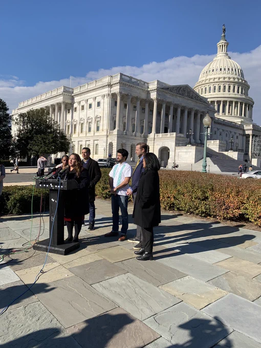 Photo of rep-elect Delia Ramirez speaking at a podium, with reps-elect Summer Lee, Robert Garcia, Greg Casar, CPC Chair Rep Jayapal, and a partner from the Economic Security Project, doing a press conference with the Capitol building behind them.