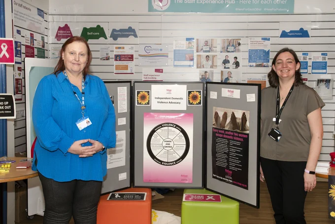 Two members of the East & North Herts Safeguarding Team are pictured stood in front of the staff experience hub at Lister Hospital in Stevenage, Hertfordshire. They were present at the hospital to lead an awareness stall engaging with visitors to promote White Ribbon Day and end violence towards women and young girls.