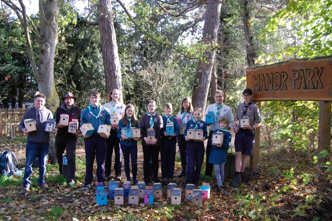 Scouts and Leaders stand with Town Council Public Realm Team holding lots of wooden bird boxes