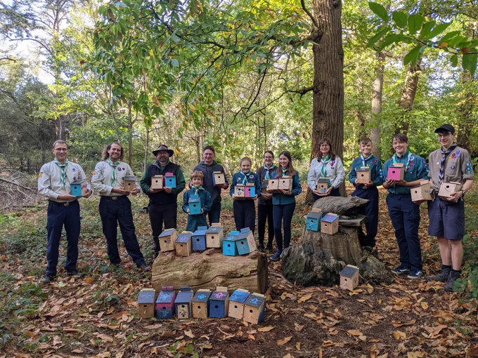 Scouts, leaders and the Town Council Public Realm Team stand in the woods holding wooden bird boxes