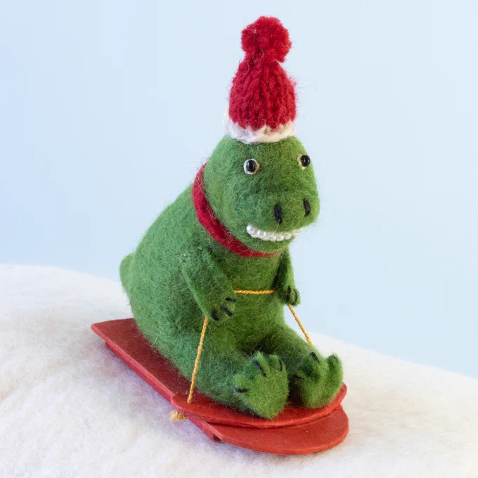 a felt T. rex wearing a Santa hat and riding a sled