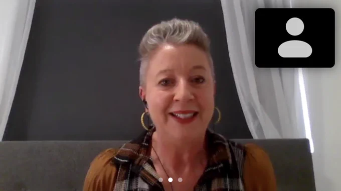 A woman with grey short hair and large gold hoop earrings smiling at the camera in a Zoom meeting.