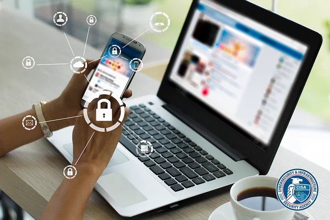 Photo of hand holding a cell phone with a laptop in the background. Icons encircling the phone represent online safety tips. CISA logo.