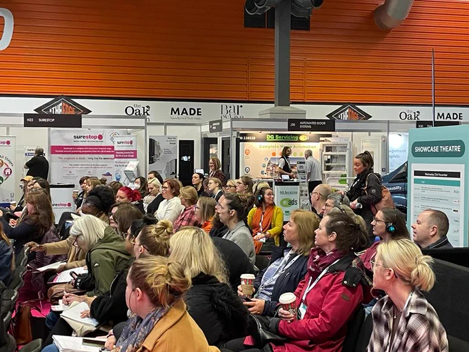 People listening to a talk at The OT Show 2022 - Automated Door Systems staff pictured in the background