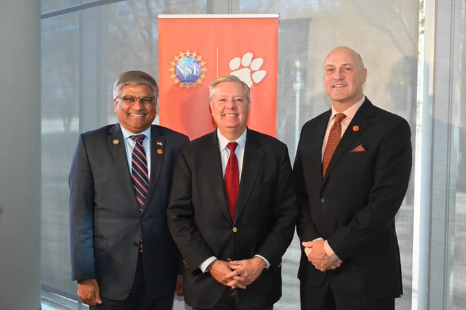 NSF Director Sethuraman Panchanathan, Senator Lindsey Graham, and President Jim Clements pose for a photo in front of an Clemson and NSF backdrop. 