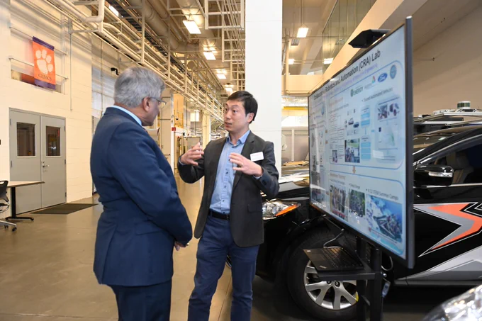 Standing in an industrial facility lined with cars, a researcher speaks with Director Panchanathan at Clemson University International Center for Automotive Research. Photo credit: Clemson University