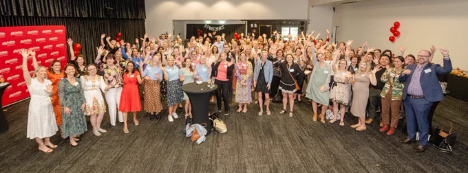 Photo of large group of people, with their hands raised and smiling, at the 10 year celebration for the Master of  Speech Pathology