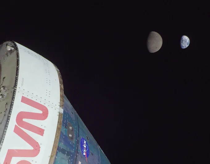 Part of the Orion spacecraft, white adapter and blue-ish Crew Module, with Moon and Earth in distance. 