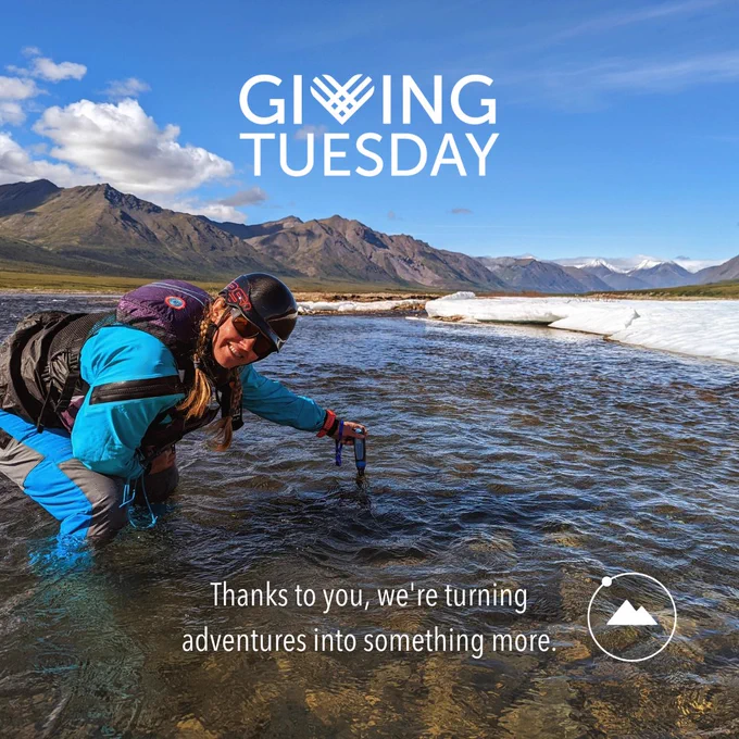 Volunteer Lindsay Hunt, sports packrafting gear while collecting data, knee-deep in the river, surrounded by mountains
