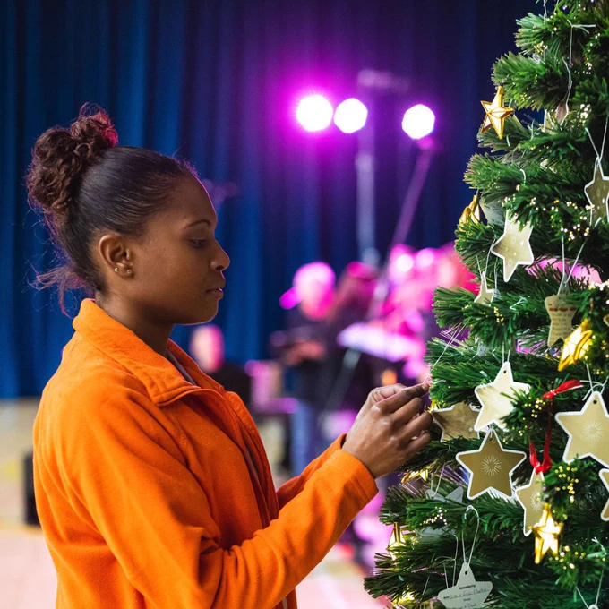 Woman in an orange St Catherine's Hospice fleece hanging gold stars on a decorated Christmas tree.
