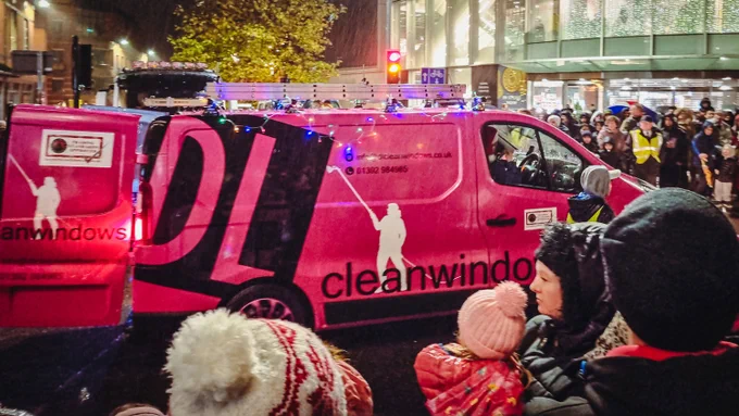 Pink van with DL Cleam Windows written on it, taking part in a parade watched by spectators