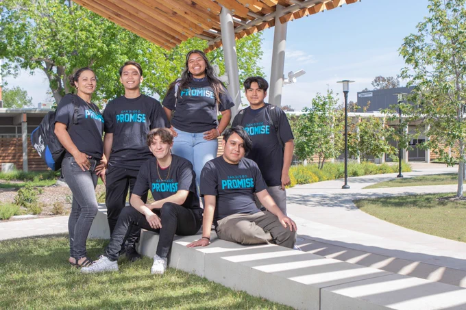 Six students wearing promise T Shirts are outside, on the grass and cement bench in the Mesa Quad.