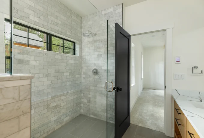 Walk in shower with gray tile and glass door built by Lexar Homes of Suncadia