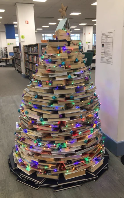 photo of stacked books made into a Christmas tree pyramid shape decorated with fairy lights