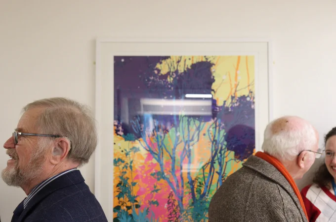 Framed art on the wall of the Emmeline Centre corridor, with event guests gathered and conversing on either side.