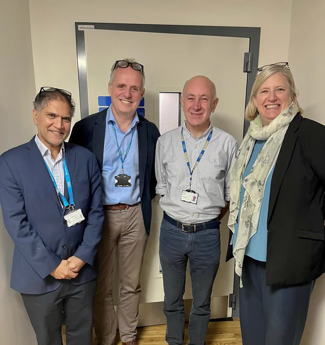 Event guests standing with CUH chair, Mike More, in front of a door in the Emmeline Centre corridor. Photo taken by Sarah Downing.