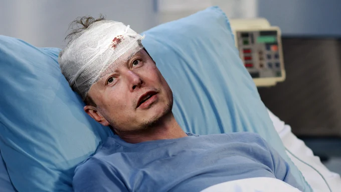 Musk in a hospital bed with bloody gauze on his forehead.