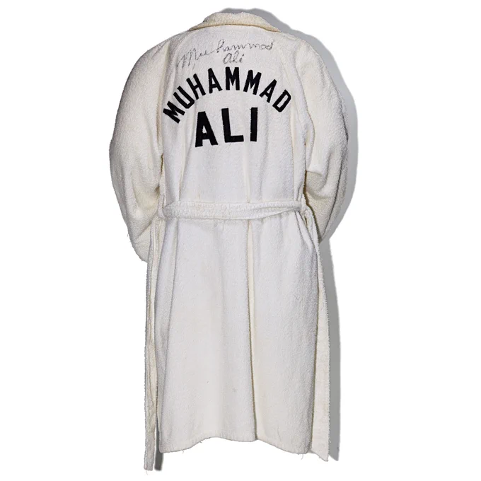 White boxing robe with text “Muhammad Ali” in all caps on back.