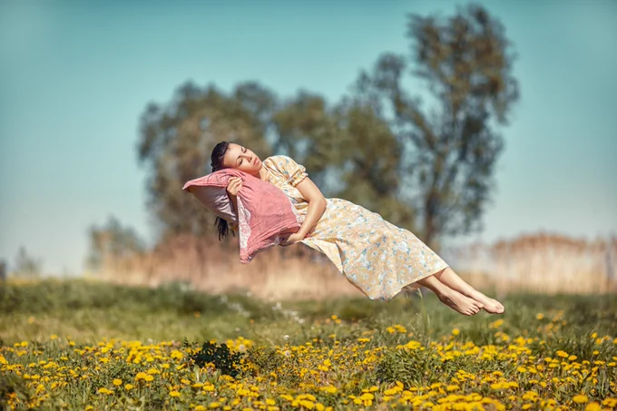 Lead image for An Introduction to the Science of Sleep - a woman with dark brown hair, sleeping on a pink pillow, floating above a meadow of yellow flowers.